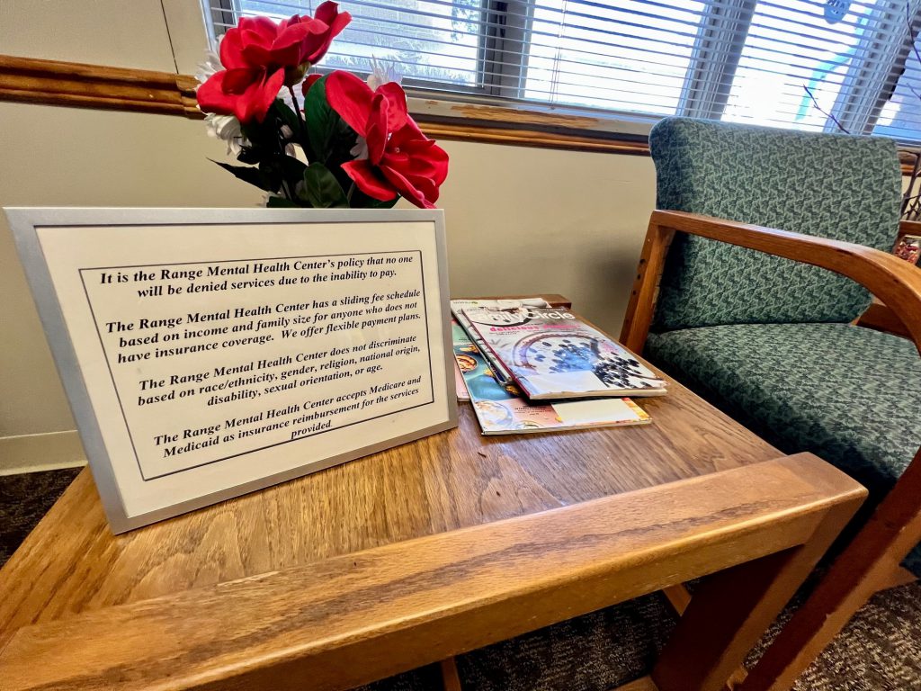 A sign stating Range Mental Health's policies sits on an old wooden end table in a lobby.