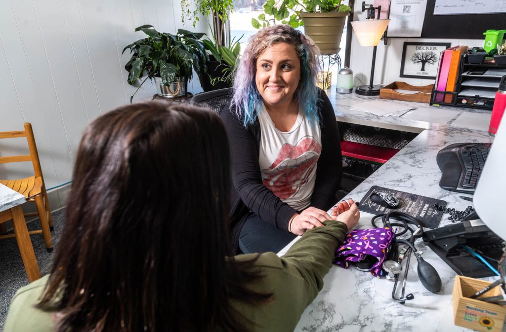 A smiling woman at a desk takes the pulse of another individual at an office.