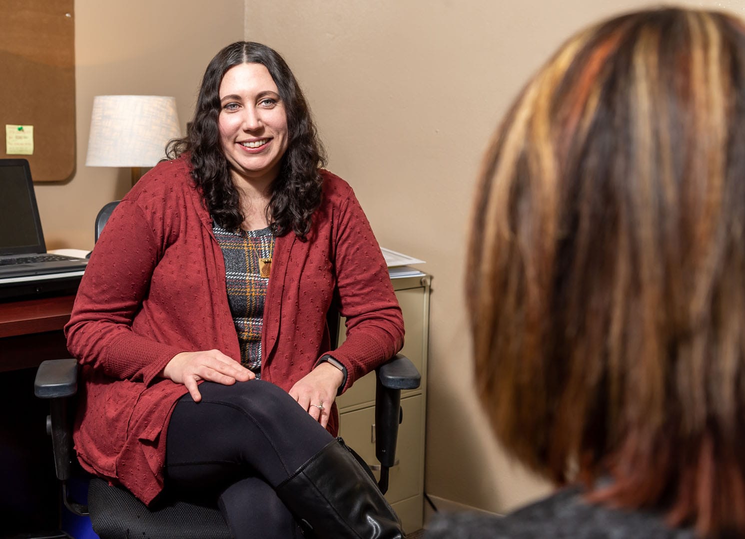 A woman looks at another smiling young woman in an office.