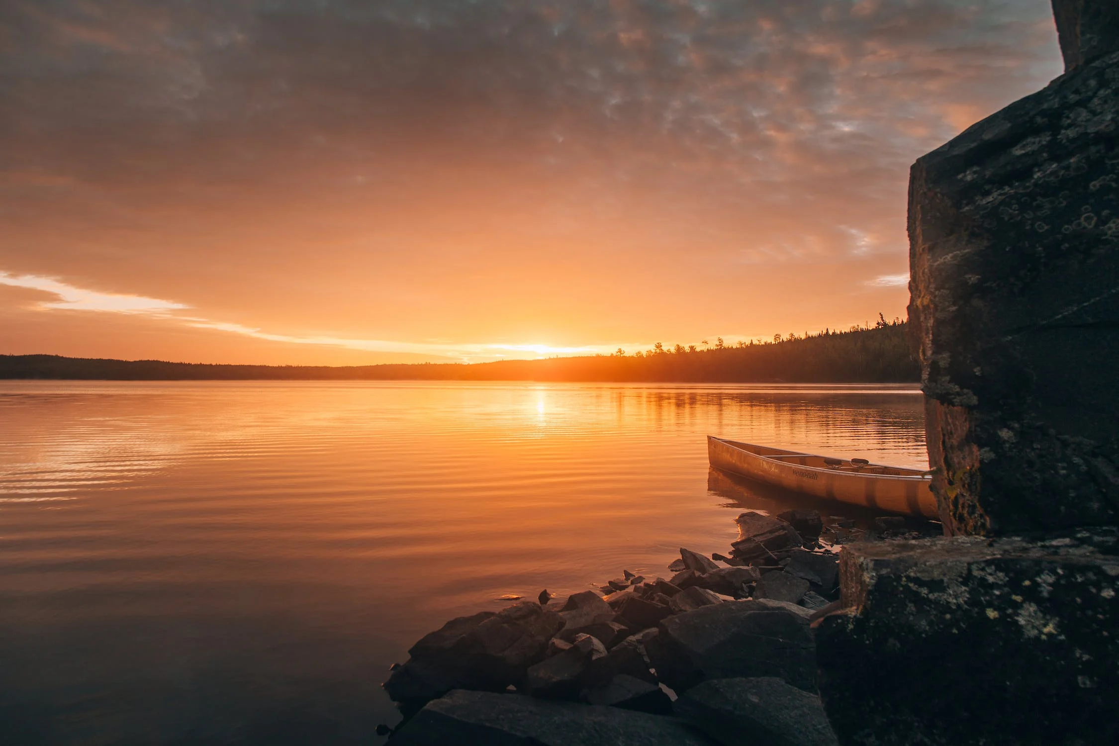 A beautiful landscape of a sunrise over a lake with a canoe.